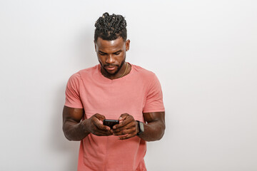 Young Man in Casual Pink Shirt Engaged With Smartphone Against Plain Background