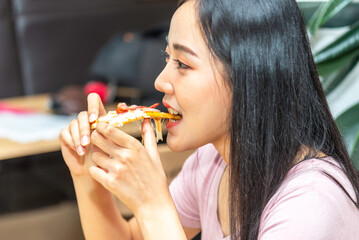 Happy caucasian young woman at modern living room and eating tasty pizza, enjoying and smiling. Fast food addiction