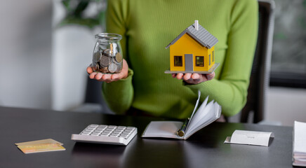 saving money, Real estate concept background. Hand of House model and coins stack on wooden table,...