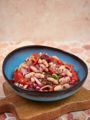 A healthy and nutritious Turkish Piyaz salad featuring white beans, tomatoes, onions, parsley, and sumac. This vegan and vegetarian dish is served in a blue bowl on a wooden board