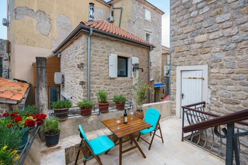 Charming balcony in a traditional stone house, featuring potted plants, a table with wine, and a picturesque view of a narrow alleyway