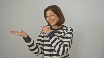 A smiling middle-aged hispanic woman in a striped sweater presents with her hand against a white background