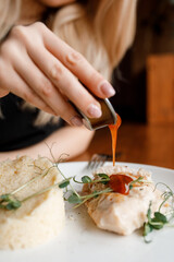sweet girl is eating а delicious dish with juicy chicken, fragrant herbs, and tomato sauce on a beautiful white plate in a cozy nice restaurant