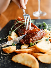 handsome man is eating a  delicious juicy steak with roasted potatoes and fresh fragrant herbs on a beautiful black board in a cozy nice restaurant