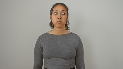 A young hispanic woman with a playful expression stands isolated against a white background,...