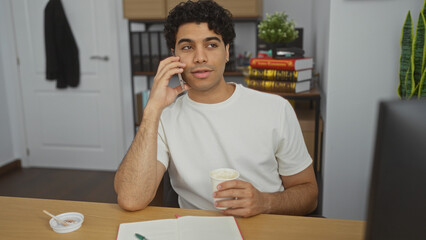 Obraz premium Handsome young hispanic man in an office with coffee and notebook, thinking while on his phone