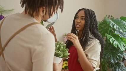 A woman and a man converse surrounded by plants in a flower shop's green interior.