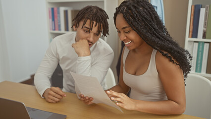 A smiling woman and a contemplative man review a document together in a modern home office setting.