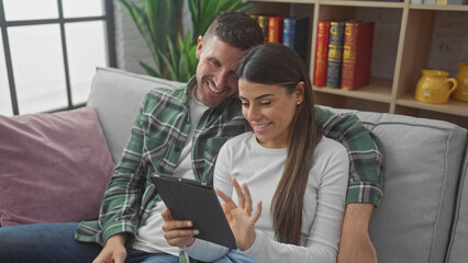 A smiling man and woman sit closely on a sofa using a tablet in a cozy living room