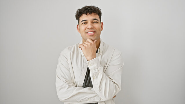 A confident young man with curly hair and a light beard poses thoughtfully in a white shirt against an isolated white background.