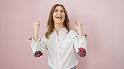 Middle-aged woman celebrating success against a pink background