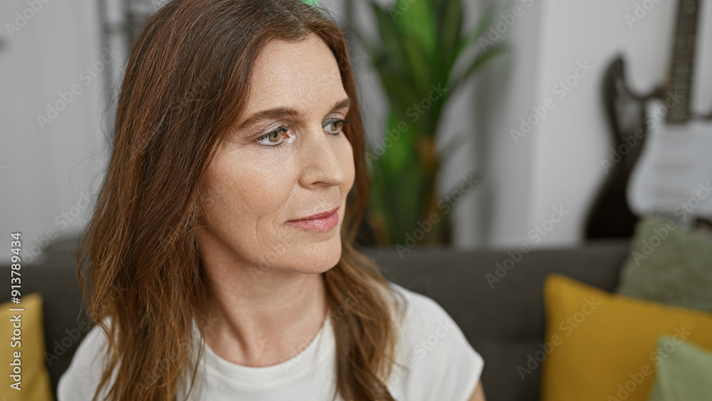 Wall mural Middle-aged woman with short hair smiling gently in a cozy modern living room, expressing serenity and comfort.