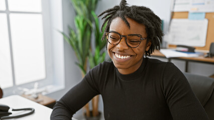 A cheerful african american woman with dreadlocks wearing glasses, enjoying her time at an office setting.