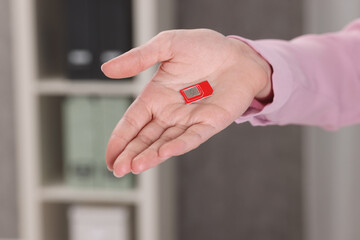 Woman holding SIM card indoors, closeup view