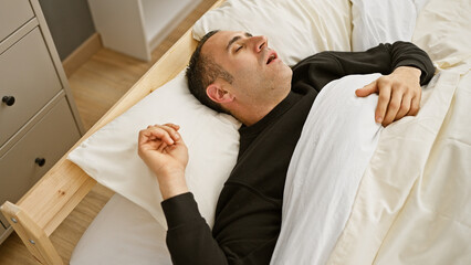 A young hispanic man sleeps soundly in a bright bedroom, adding a peaceful vibe.