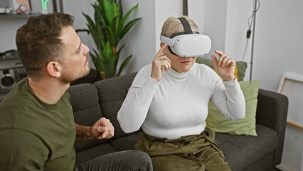 A man observes a woman experiencing virtual reality in a modern living room, evoking technology, leisure, and innovation.