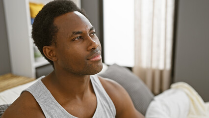 Portrait of a thoughtful young man sitting in a modern bedroom with natural light streaming in.