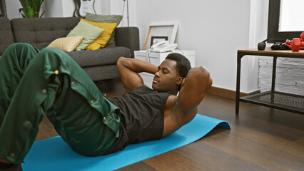 African american man exercising on a blue yoga mat in a modern living room interior, maintaining fitness.