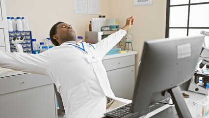 Fototapeta premium African man stretching in a modern laboratory setting, surrounded by scientific equipment, indoors.