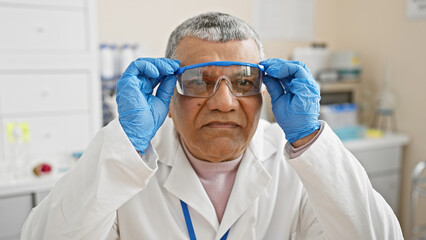 Naklejka premium A mature man scientist adjusts protective goggles in a laboratory setting.