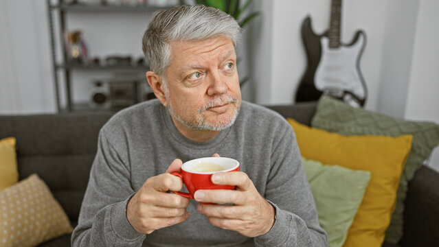 Mature man holding coffee cup in modern living room with guitar in background