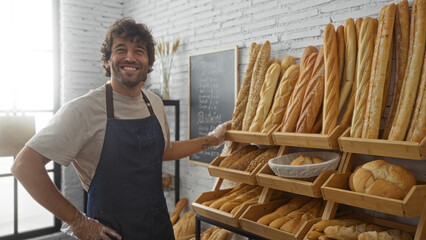 Young man smiling indoors at a bakery surrounded by freshly baked bread in the sunny shop interior