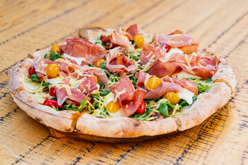Gourmet pizza with prosciutto, cherry tomatoes and arugula on rustic wooden table