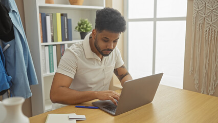 Focused african man using laptop in a modern indoor home office setting