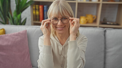 Smiling woman wearing glasses sitting comfortably on a sofa in a cozy living room setting