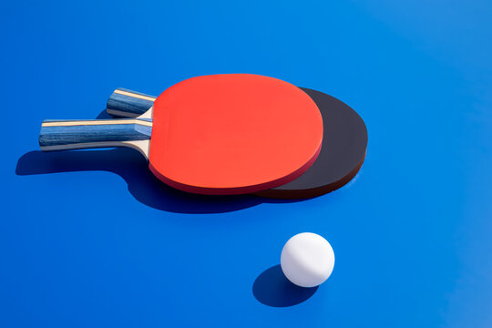 Red and black table tennis paddles with ball on blue background