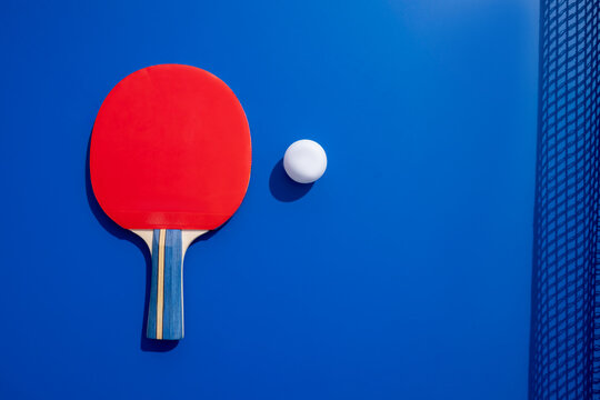 Vibrant red table tennis paddle and ball against blue backdrop