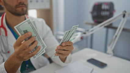 Handsome bearded man in a hospital counting us dollar bills in an indoor clinic setting.