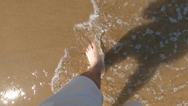 Pies de hombre cauc&aacute;sico andando sobre la fina arena de la playa de Tazones y ba&ntilde;ado por las aguas del litoral Cant&aacute;brico, norte de Espa&ntilde;a