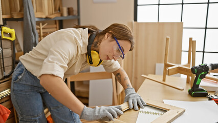 A young brunette woman meticulously measures wood in a well-lit carpentry workshop, exuding focus...