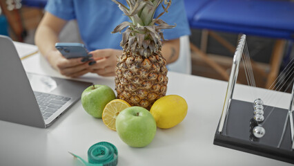 A focused healthcare worker handles a smartphone amidst a workspace with fruit and a newton's...