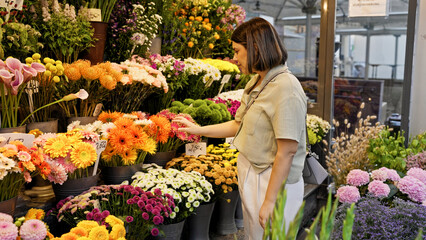 Young beautiful hispanic woman touching colourful flowers in the streets of Vienna