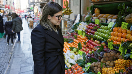 A brunette woman examines fresh produce at a vibrant istanbul street market, showcasing urban turkish life.