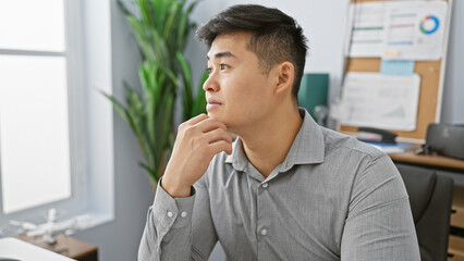 Pensive asian man contemplating in a modern office setting, embodying professionalism and...