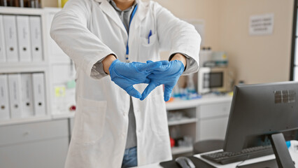 Naklejka premium A young asian man in a lab coat putting on blue gloves in a laboratory setting.