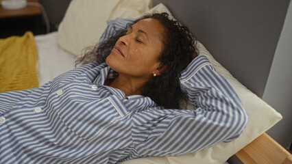 Woman relaxing indoors with eyes closed on bed in bedroom wearing striped pajamas