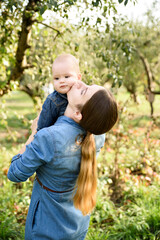 Fototapeta premium mother kisses her baby holding in orchard. Both are dressed in denim, creating cozy and loving scene that captures warmth of family moments in nature. Mother and child.