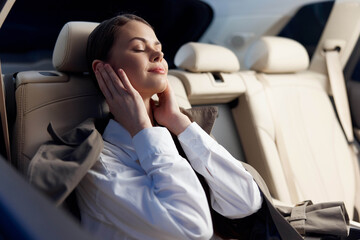 Woman in car back seat resting her head on her hand, appearing deep in thought, with overcast skies...