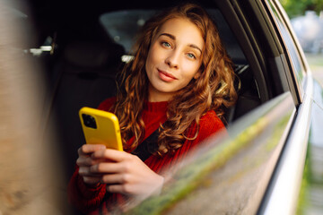 Passenger woman with phone in the back seat of a car. Concept of technology, internet, blogging, traveling by car, business.