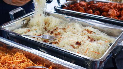 A close-up shot of stir-fried rice noodles in a serving dish. The noodles are white and translucent, and they are mixed with fried onions and other ingredients. Close-up of Noodles in a Serving Dish.