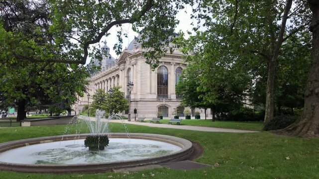 Petit Palais art museum side building through tree leaves with the surrounding park and fountain in Paris, France.