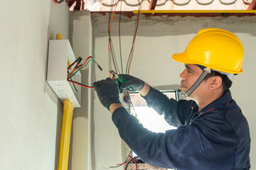 An electrician in a high-visibility vest works on wiring at a construction site.