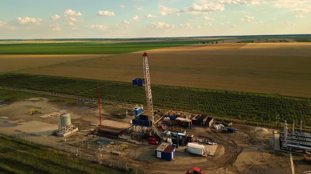 Aerial shot of shale gas drilling rig in a rural field in Romania. Fracking drill seen from above in the middle of a crop field. Drone footage of Hydraulic fracturing construction site.
