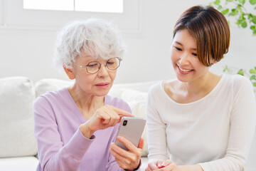 母親にスマートフォンの操作を教える娘　リビングルーム