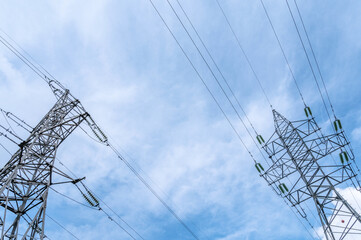 Two electricity pylons with power lines against blue cloudy sky