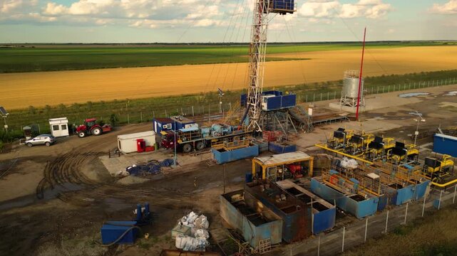 Aerial shot of shale gas drilling rig in a rural field in Romania. Fracking drill seen from above in the middle of a crop field. Drone footage of Hydraulic fracturing construction site.
